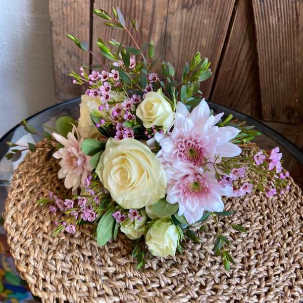 Low arrangement of cream roses and pale pink mums with tiny pink blossoms on a woven mat