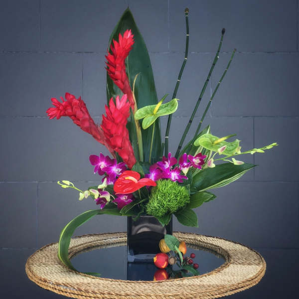 Tropical floral arrangement with red ginger, orchids, and anthurium in a black vase