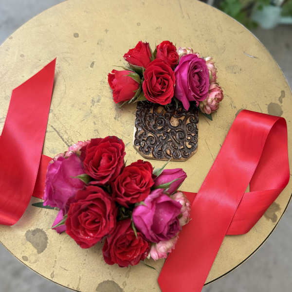 Two rose wrist corsages with red ribbon on a gold surface