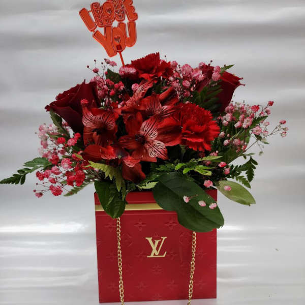 Red floral arrangement in a branded gift bag with an "I love you" topper
