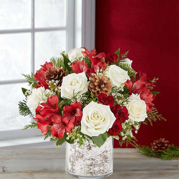 Red and white floral arrangement in a silver vase with pinecones