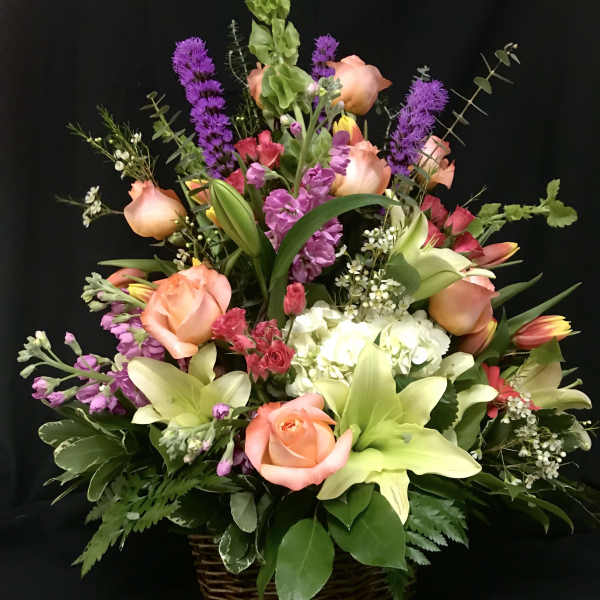 Mixed bouquet in a wicker basket with peach roses, lilies, and purple spikes