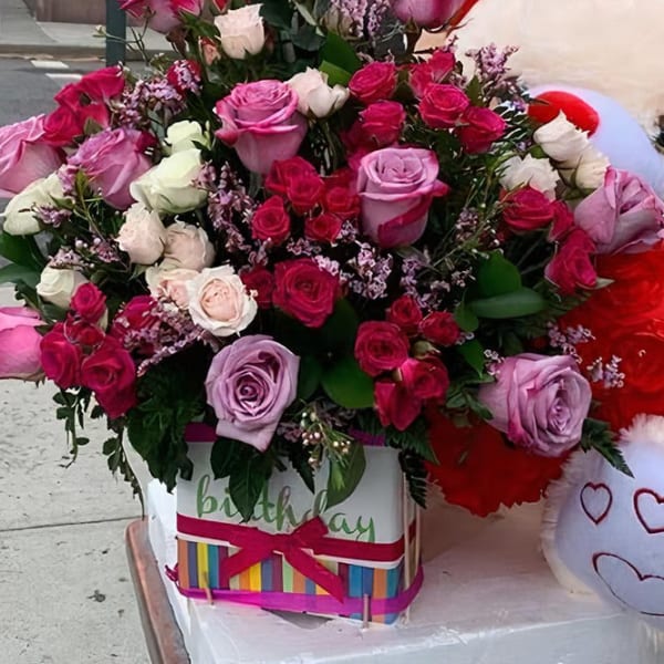 Pink and red rose bouquet in a birthday box beside a teddy bear
