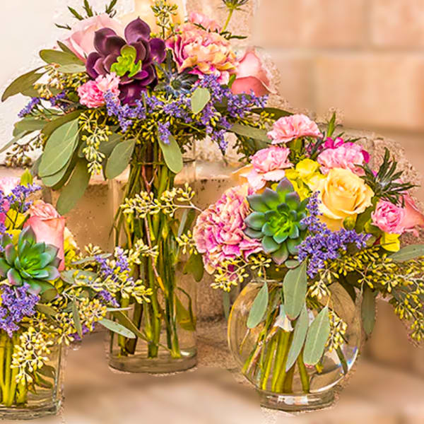Three colorful floral arrangements in glass vases with succulents