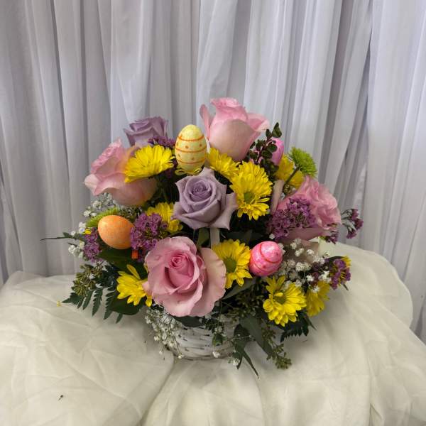 Basket arrangement of pink and lavender roses with yellow daisies and Easter eggs