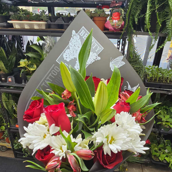 Handheld bouquet of red roses, white daisies, lilies, and alstroemeria in gray paper wrap