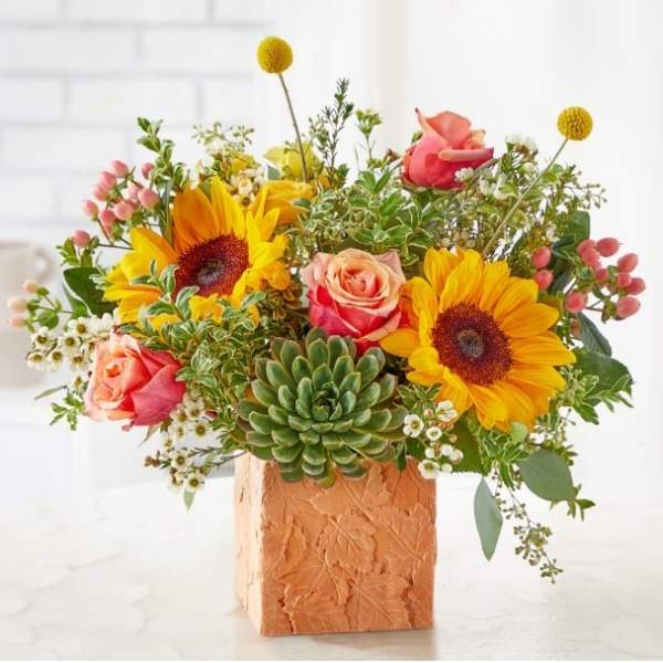 Mixed bouquet with sunflowers, roses, and a succulent in a textured square vase