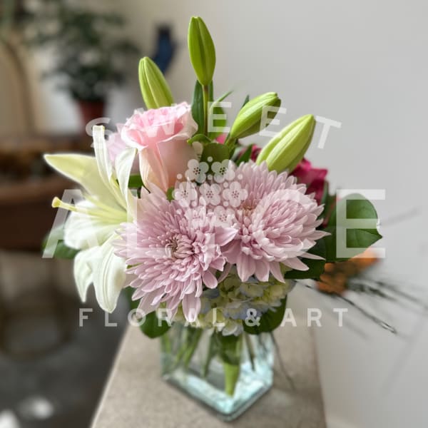 Pink chrysanthemums and lilies in a clear glass vase