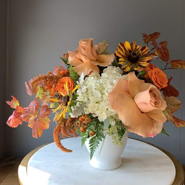 Peach roses and white hydrangeas in a white vase with autumn leaves