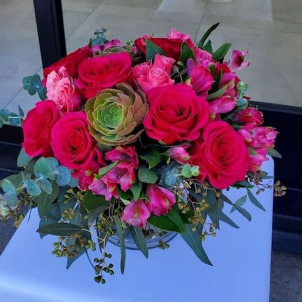 Low arrangement of bright pink roses and alstroemeria with a green succulent in a clear glass vase