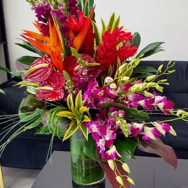 Tall tropical arrangement with purple orchids, red anthuriums and orange flowers in a clear glass vase