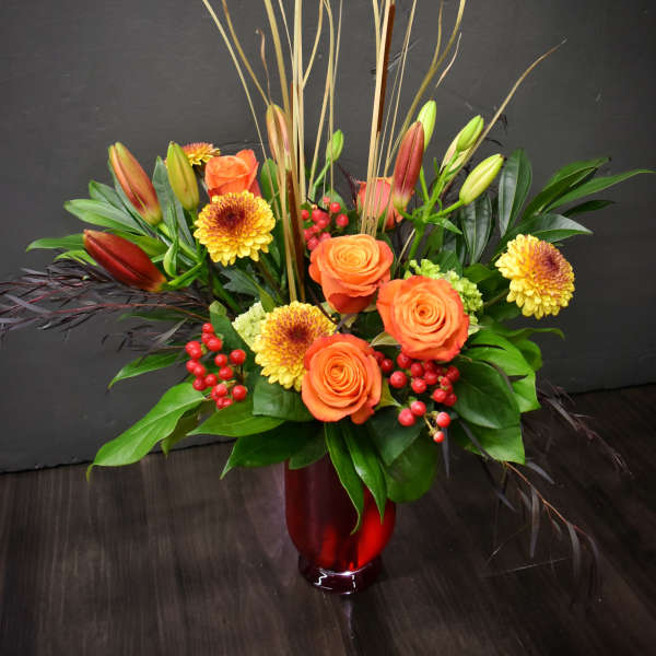 Orange roses and yellow chrysanthemums in a red vase with tall reeds