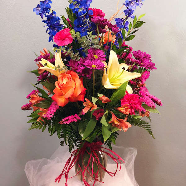 Colorful bouquet with blue delphinium, orange roses, and yellow lilies in a vase