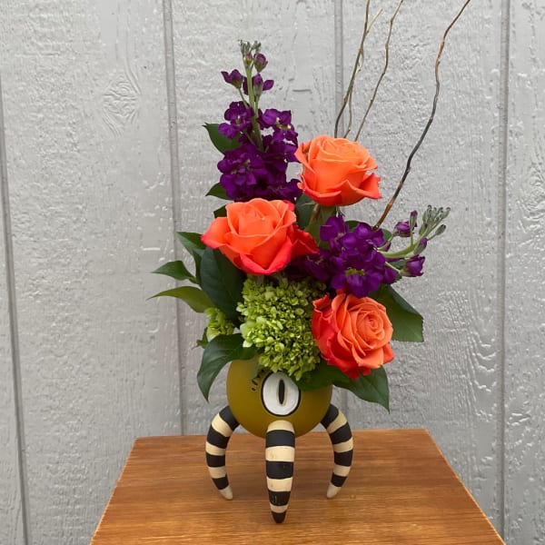 Orange roses and purple flowers arranged in a decorative vase with striped legs.