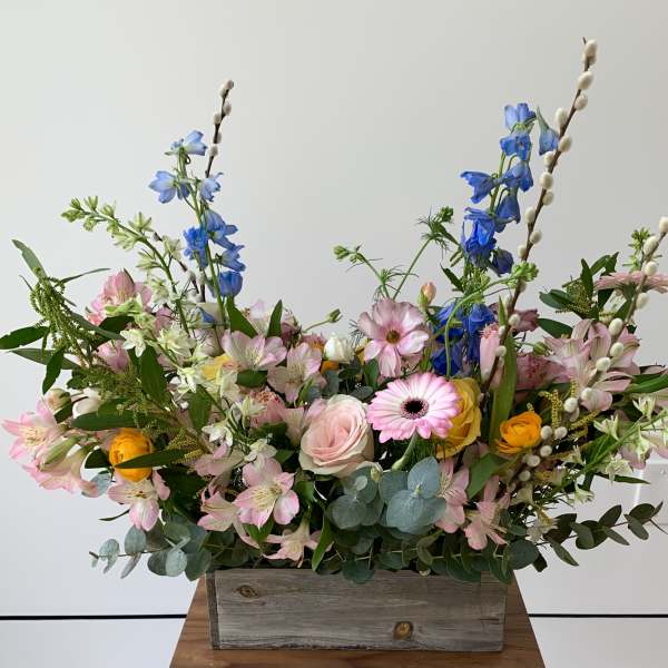 Mixed bouquet in a rustic wooden box with pink, blue, and yellow flowers