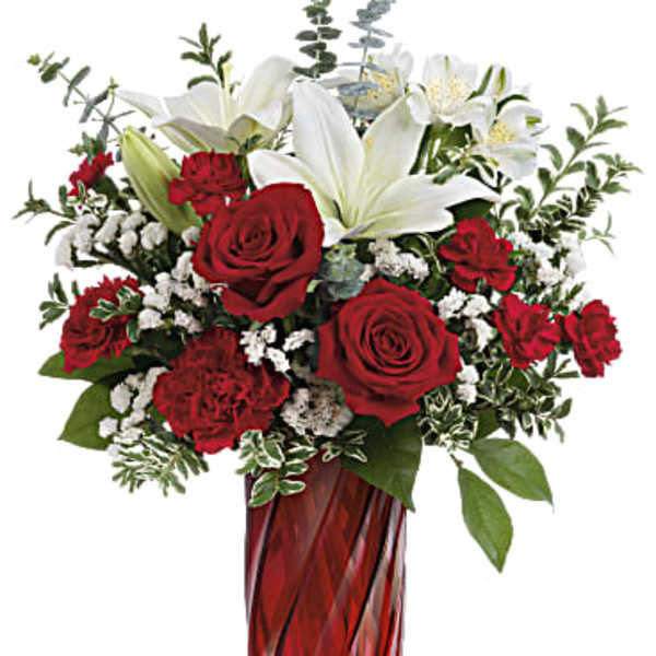 Tall red and white arrangement with roses, carnations, and lilies in a red glass vase