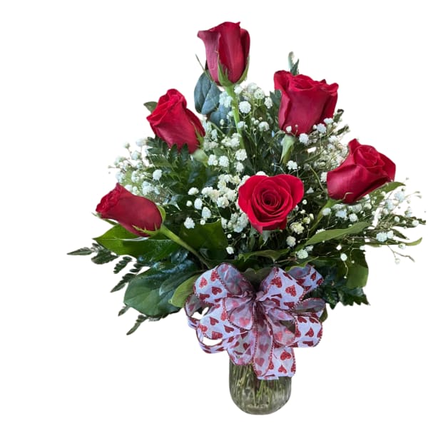 Arrangement of red roses and white filler flowers in a glass vase with a heart-pattern bow