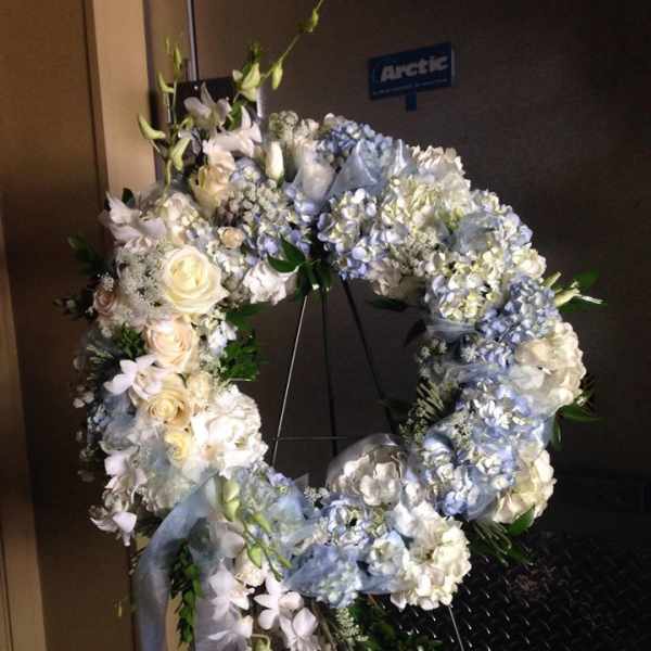 Large circular floral wreath with pale blue and white flowers on a stand
