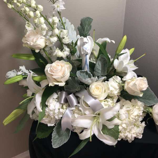White floral arrangement with lilies, roses, and ribbon in a vase
