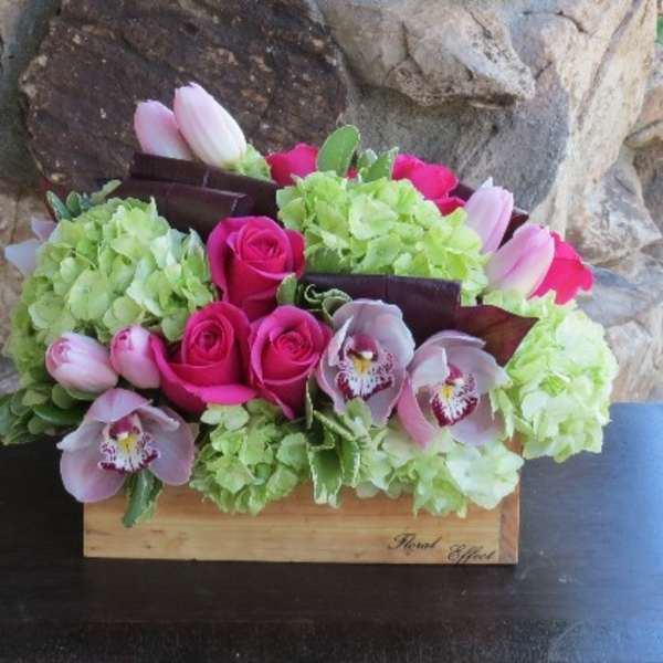 Bouquet of pink roses, tulips, and orchids in a wooden box