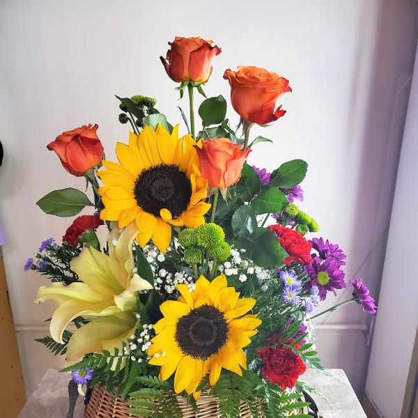 Basket arrangement with sunflowers, orange roses, and mixed daisies