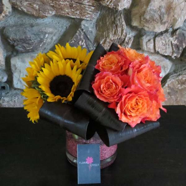 Sunflowers and orange roses in a black-wrapped vase arrangement