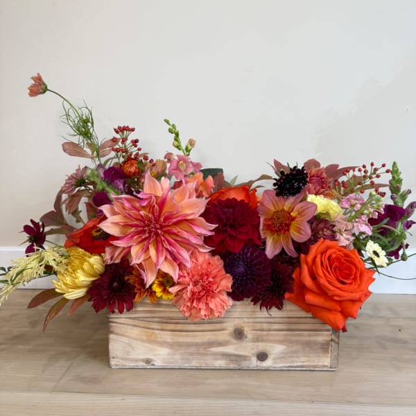 Mixed flower arrangement in a wooden box with orange and pink blooms