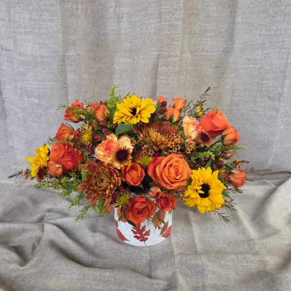 Orange and yellow flower arrangement in a white vase with leaf print