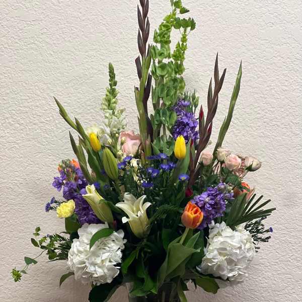 Tall mixed bouquet in a clear glass vase with white, purple, yellow, and orange blooms