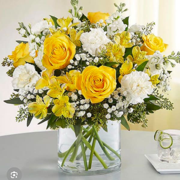 Yellow roses and white flowers arranged in a clear glass vase