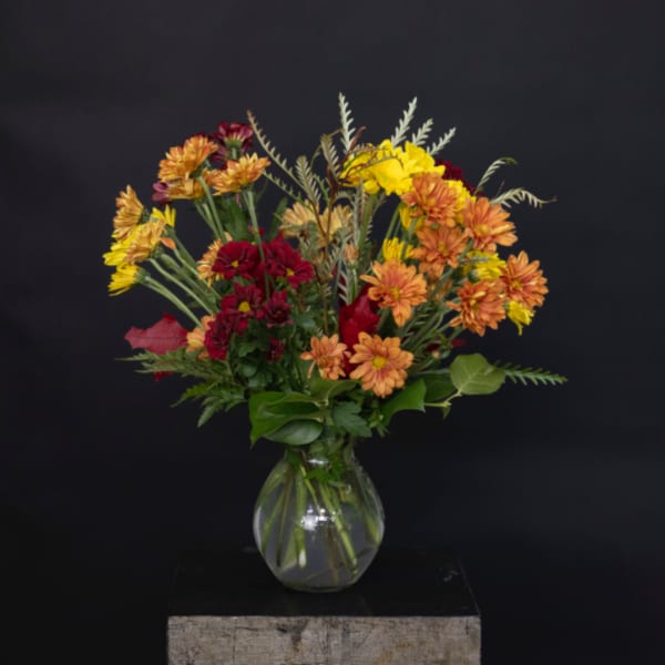 Mixed bouquet of orange, yellow, and red flowers in a clear glass vase