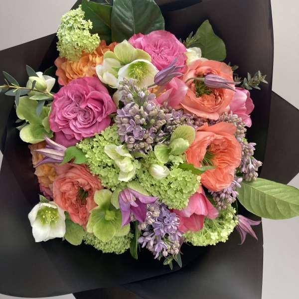 Mixed bouquet of pink, coral, and green flowers wrapped in black paper