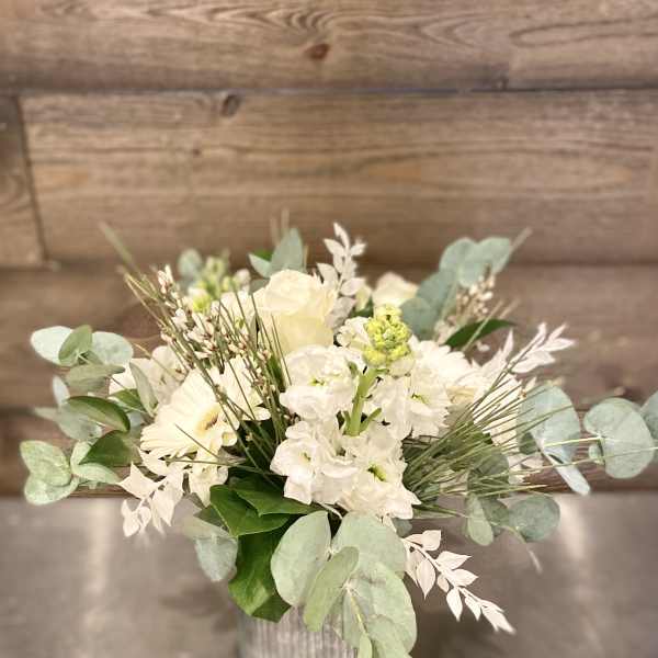 White floral arrangement in a ribbed metal vase with pale greenery