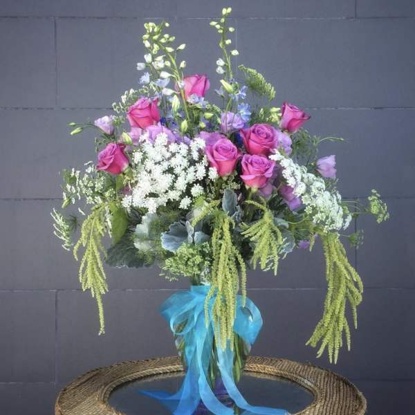 Pink roses and lavender flowers in a glass vase with a blue ribbon