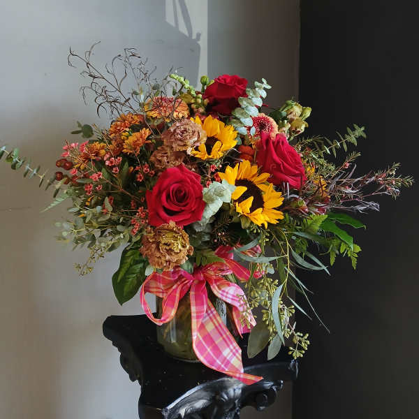 Bouquet of red roses and sunflowers in a glass vase with a pink ribbon