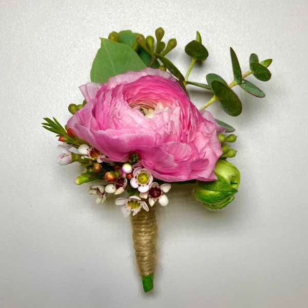 Pink ranunculus boutonniere with small white blossoms and greenery