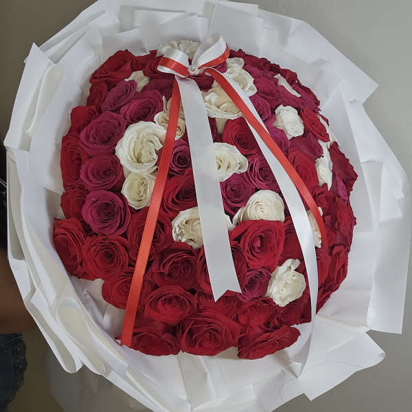 Round bouquet of red and white roses wrapped in white paper with a ribbon