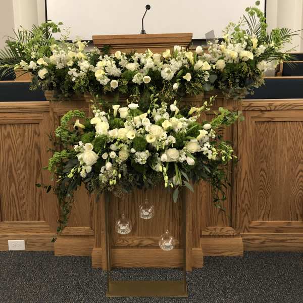 Large white floral arrangement on a podium with hanging glass ornaments