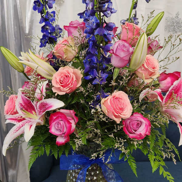 Tall bouquet of pink roses, lilies, and blue delphinium in a glass vase