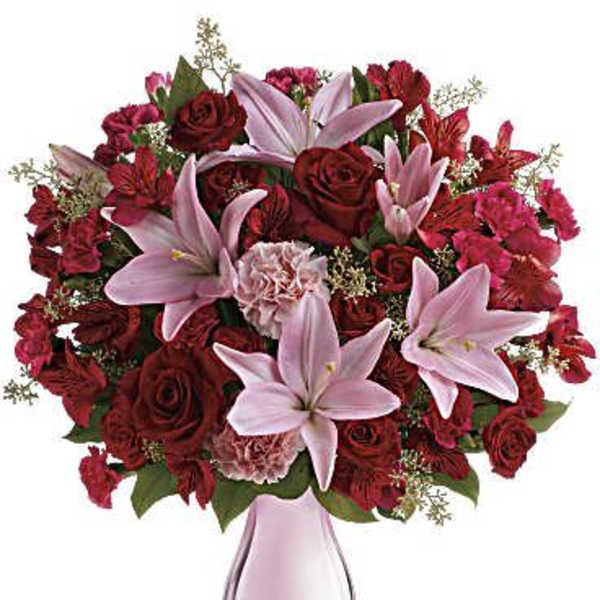 Pink lilies and red roses arranged in a pink glass vase