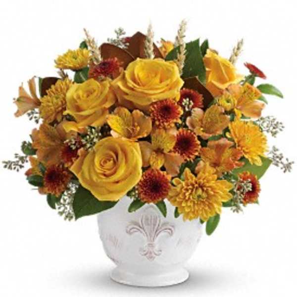 Low round arrangement of yellow roses and orange mums in a white ceramic bowl