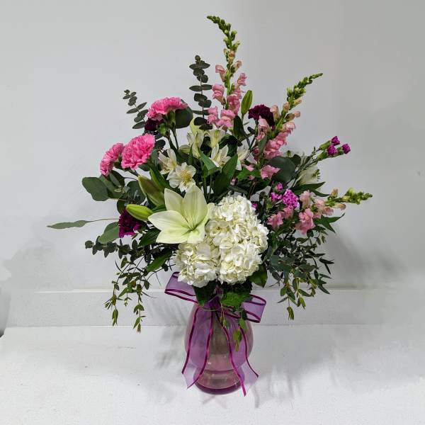 Mixed pink and white flowers in a glass vase with a purple ribbon
