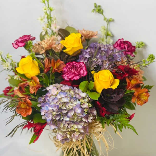 Mixed bouquet of roses, hydrangeas, and carnations in a glass vase