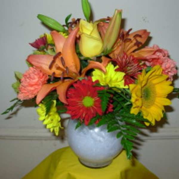 Mixed bouquet of lilies, roses, and daisies in a white vase