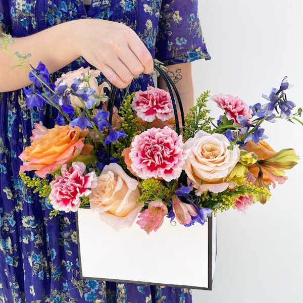 Handheld floral arrangement in a white box bag with roses and carnations