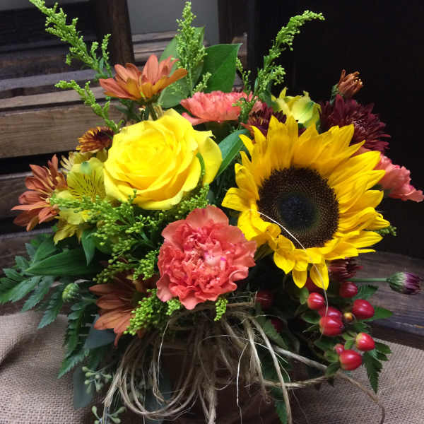 Mixed bouquet with a sunflower, yellow rose, and pink carnation in a rustic container