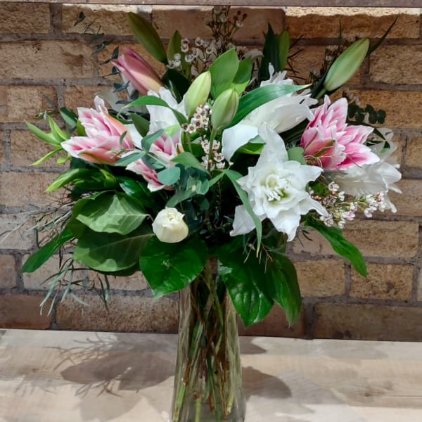 Pink and white lilies arranged in a clear glass vase