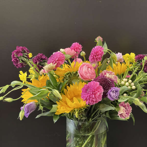 Mixed bouquet of pink, yellow, and purple flowers in a glass vase
