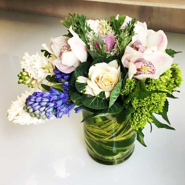 Mixed bouquet with orchids, roses, and blue flowers in a glass vase
