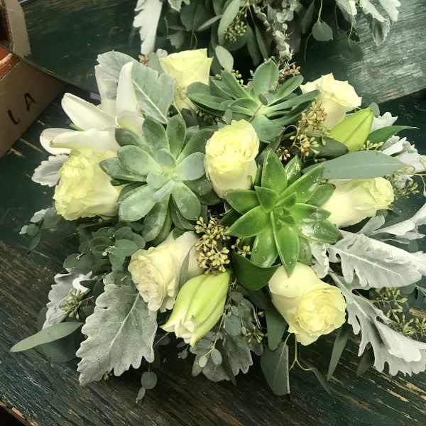 Two pale yellow rose and succulent bouquets on a dark table